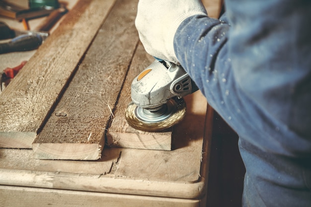 Man timmerman freest het stuk hout door een slijpmachine in zijn eigen werkplaats