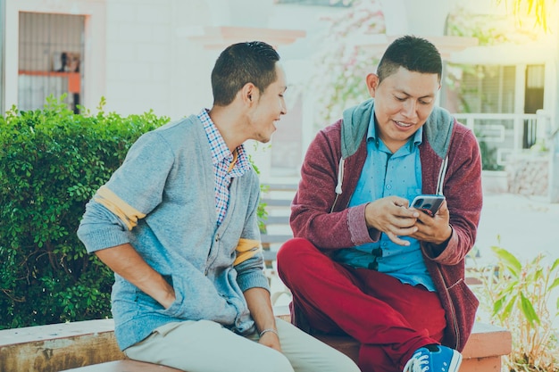 Man toont zijn mobiele telefoon aan een andere man twee jongens die hun mobiele telefoons controleren Twee jonge mannen die hun mobiele telefoons vergelijken