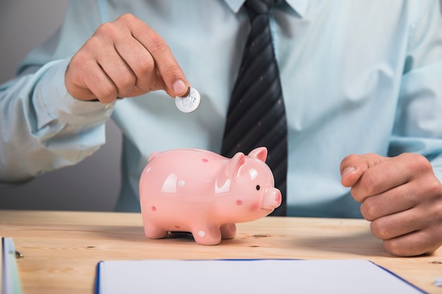 A man tosses a coin into a piggy bank