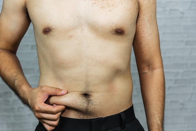 Man touching his fat belly on gray background