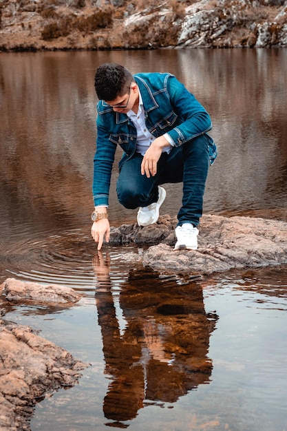 Man touching the water of a lake looking at his reflection