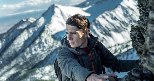 写真 トップの雪に覆われた山々に岩の上をクロール男観光客。動機と目標の達成