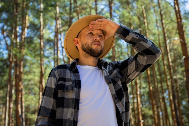 Man tourist in hat and plaid shirt in the woods.