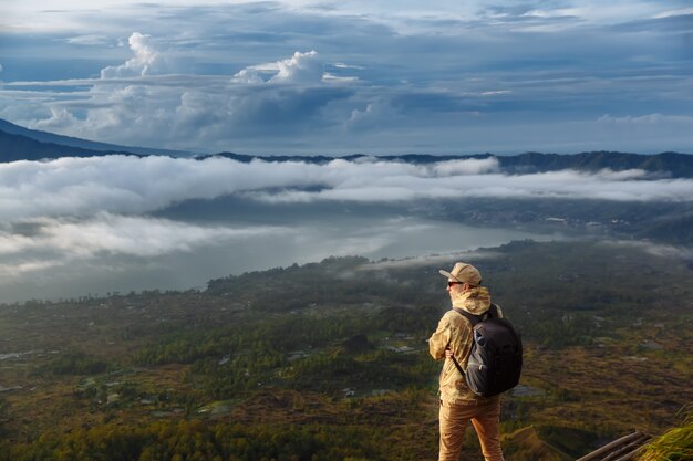 Man tourist looks at the sunrise on the volcano Batur on the island of Blai in Indonesia. Hiker man with backpack travel on top volcano, travel concept