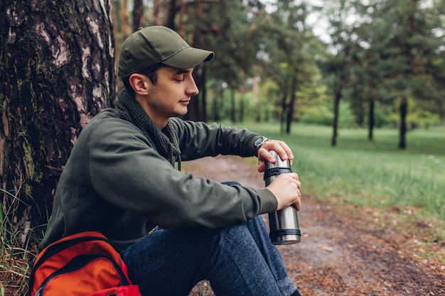 Man tourist opens thermos with hot tea in spring forest Camping, traveling