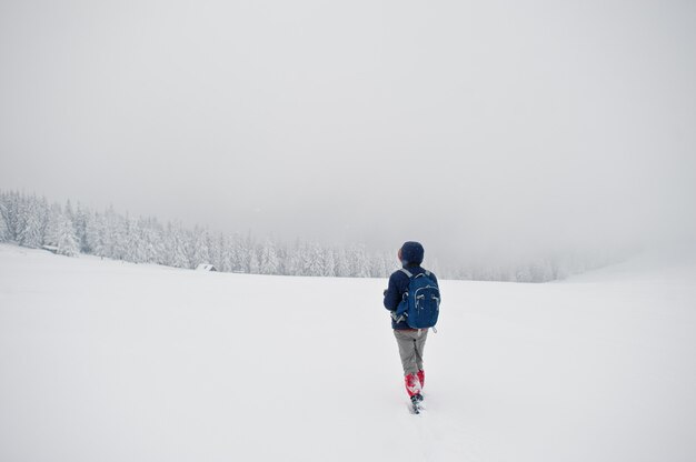 雪に覆われた松の木の山で、バックパックを持つ男観光写真家