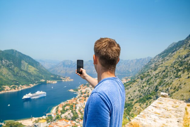 Турист фотографируется на смартфоне, стоя на горе Ловцен над заливом Котор и старым городом