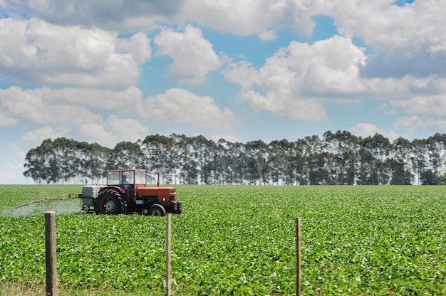 Man on a tractor watering soybean plantations in fields of Uruguay A group of trees can be seen on