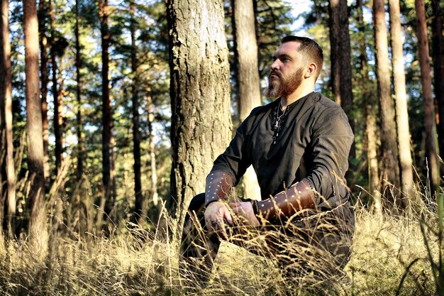 Foto uomo in abiti tradizionali in ginocchio sul campo contro gli alberi