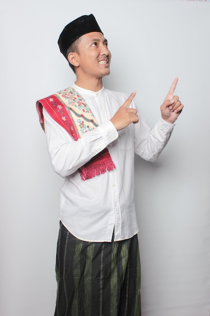 A man in a traditional malay outfit points his finger at the top of his shirt.