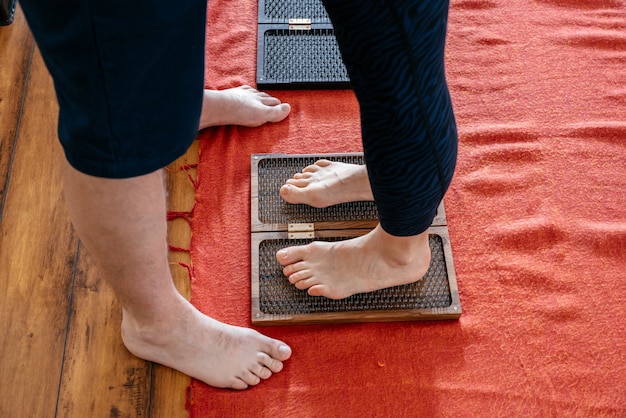 Man trainer helpt vrouw om op sadhoe yoga bord te staan, blootsvoets op een spijkerbed