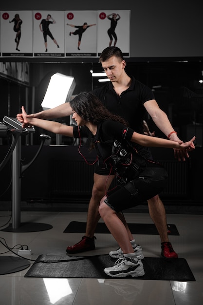 Man trainer trains a girl in an EMS suit in the gym