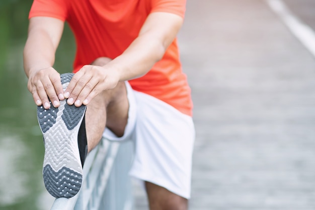 Man training en wellness-concept: de Aziatische atleet warmt zijn lichaam op voordat hij op de weg in het park begint te rennen.