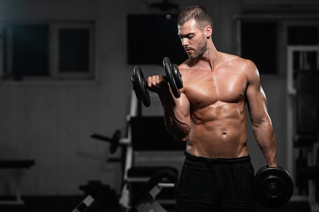 Man trains in the gym. Athletic man trains with dumbbells, pumping his biceps