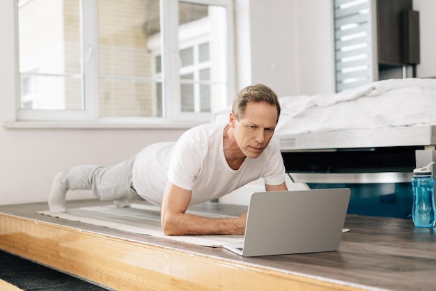 Man traint op fitnessmat terwijl hij online kijkt terwijl hij traint op laptop