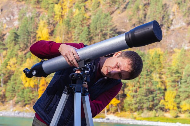 写真 男性旅行者は腰をかがめ、三脚に望遠鏡を設置して秋の風景と星を調査します