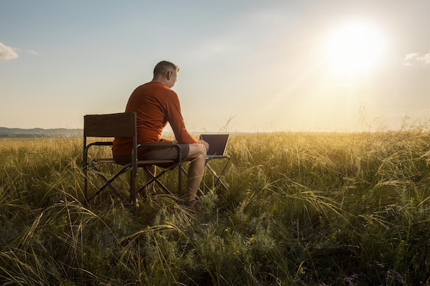 man traveler blogger work remote on netbook computer while enjoying beautiful nature landscape view outdoors at sunset