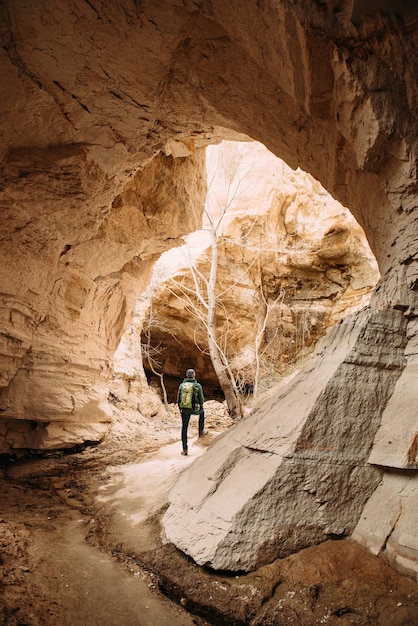 Man traveler exploring Cappadocia sandstone caves on the way to Rose Valley. Panorama of tunnel with tourist and sunlight. Beautiful Goreme landscape in Turkey.