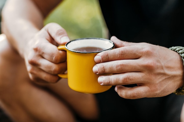 Photo man traveler hands holding a cup of tea outdoors the concept of adventure travel tourism and camping tourist drinking tea from a mug in the camp