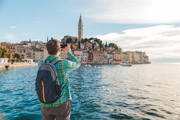 Man traveler looking at rovinj city from the harbour taking picture on the phone