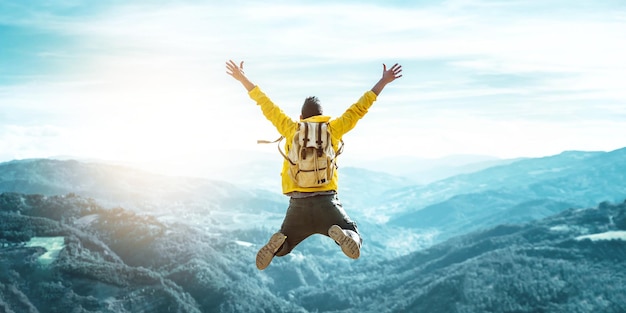 Man traveler on mountain summit enjoying nature view with hands raised over clouds