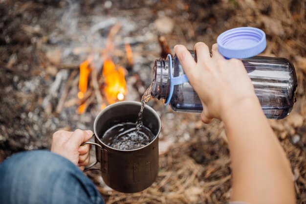 Man traveler pours water from a bottle into a metal mug