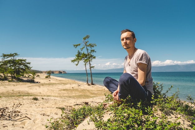 Man traveler relaxing on the beach of Olkhon island overlooking the water of the lake and the mountains and the blue sky