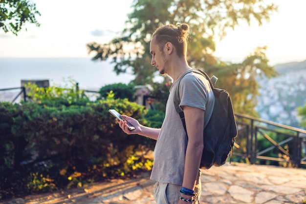 彼のスマートフォン、自然、山を見てバックパックを持つ男旅行者