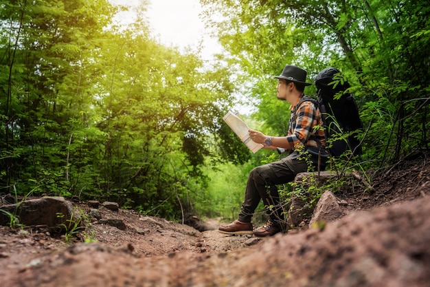 Man traveler with backpack sitting and reading map in the forest