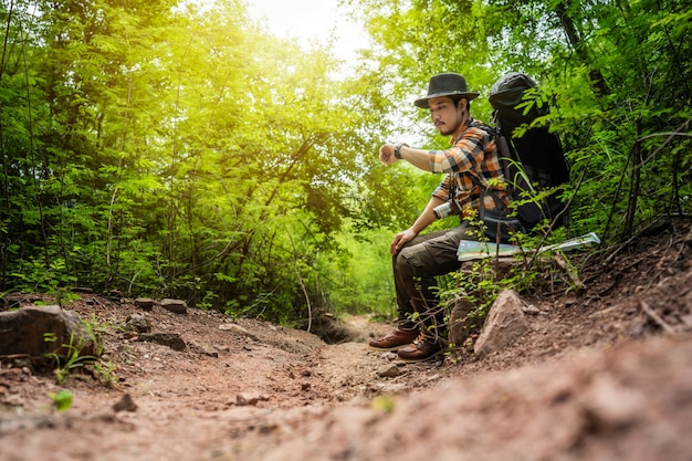 Equipaggi il viaggiatore con lo zaino che pensa e che guarda un orologio nella foresta