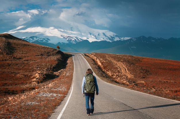 Il viaggiatore dell'uomo con lo zaino cammina lungo la strada in montagna