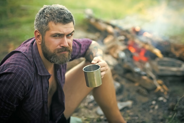 Man traveler with cup relax at bonfire on nature.