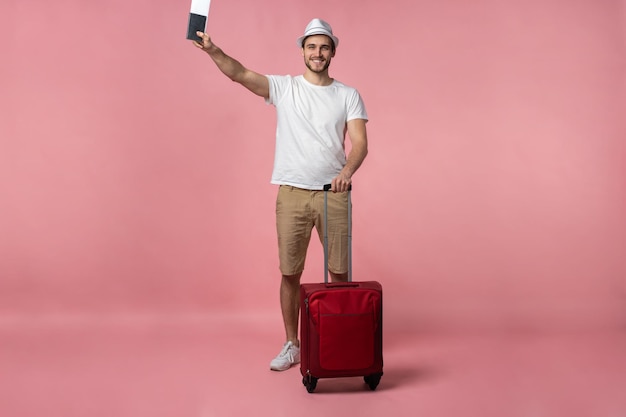 色の背景にスーツケース、パスポート、チケットを持つ男の旅行者。