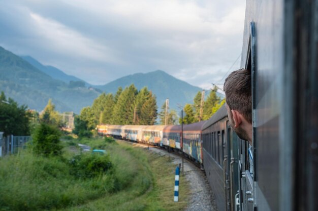 Foto uomo che viaggia in ferrovia attraverso i balcani bel giovane che guarda fuori dalla finestra del treno turista