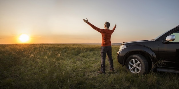 man traveling exploring enjoying the view of the nature at sunrise man standing near his car on vacation and watching the sunset at nature