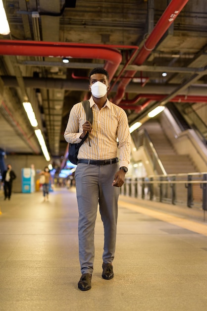 Man traveling and waiting at train station during covid and wearing face mask while social distancing and walking