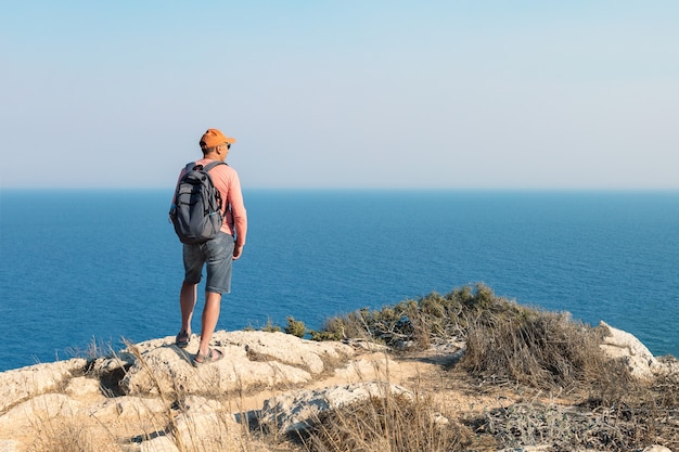 Man traveling with backpack hiking in mountains and looking on sea landscape. Active healthy lifestyle adventure journey vacations.