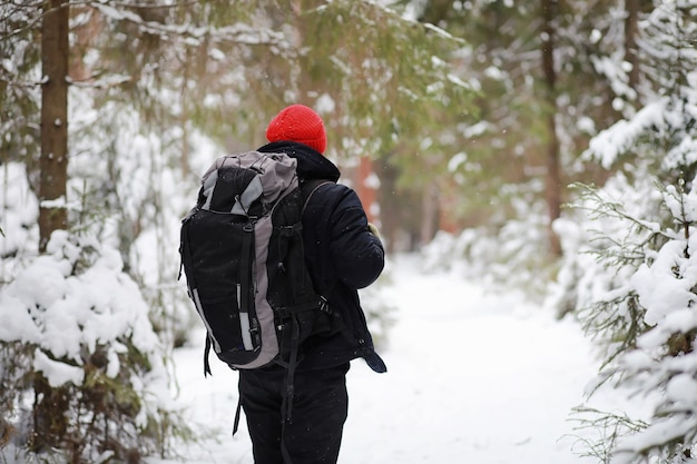 A man travels with a backpack. Winter hike in the forest. Tourist on a walk in the winter in the park.