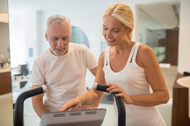 Uomo su un tapis roulant e istruttore femminile alla ricerca durante l'accensione della macchina da palestra