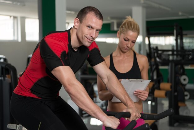 Man trein fiets op machine met personal trainer