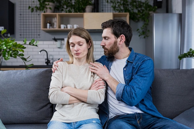 Мужчина пытается поддержать и успокоить грустную женщину супружескую пару, сидящую дома на диване