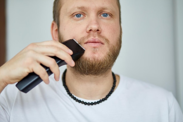 Foto uomo che taglia la barba con un tagliacapelli elettrico in un ambiente interno ben illuminato