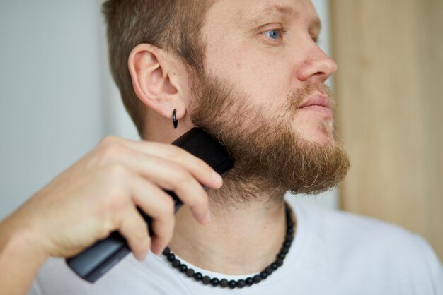 Foto uomo che taglia la barba con un tagliacapelli elettrico in un ambiente interno ben illuminato