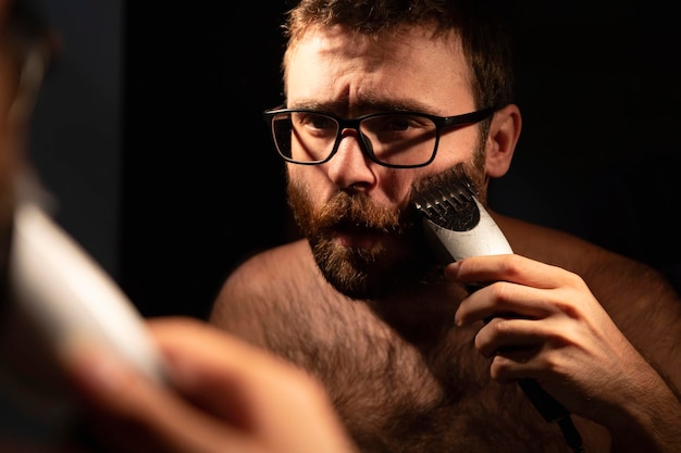 A man trims his beard in front of the mirror