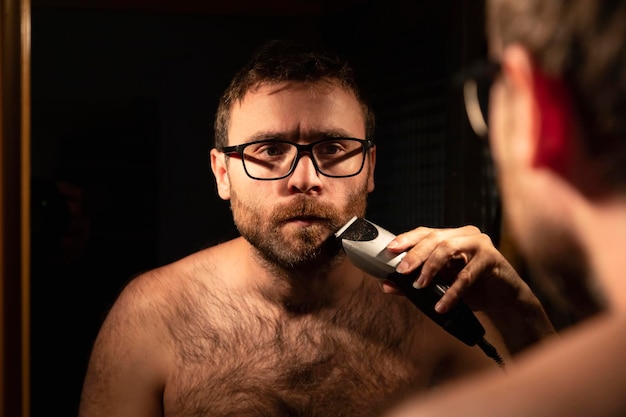 Foto un uomo taglia la barba davanti allo specchio