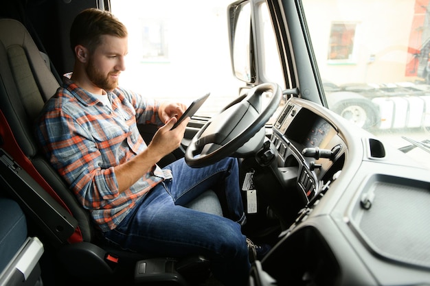 man truck driver sitting behind wheel of car and holding digital tablet in his hands