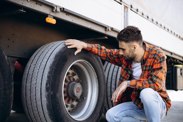 写真 彼のトラックの車輪をチェックする男性トラック運転手