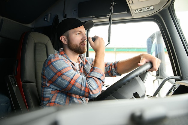 Foto camionista uomo che guida in una cabina del suo camion e parla al trasmettitore radio