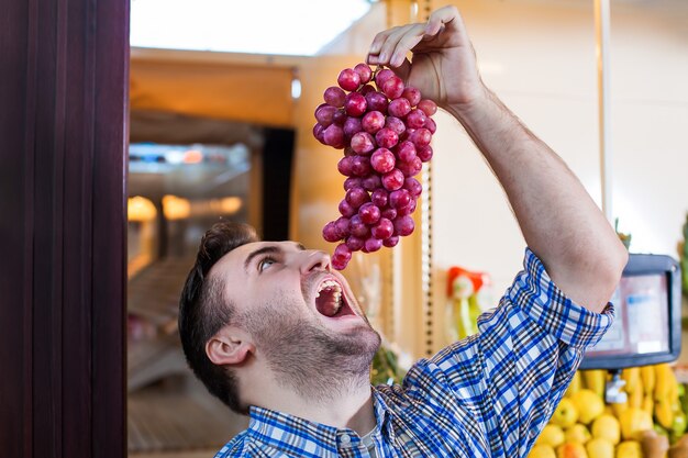 Foto uomo che cerca di mangiare un grappolo d'uva.