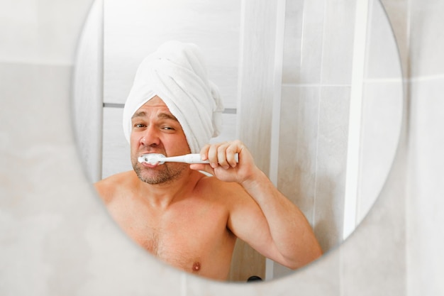 A man in a turban made of a towel on head brushes teeth after a morning shower